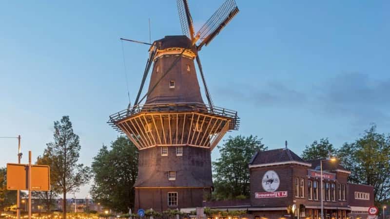 Amsterdam, Netherlands - May 16, 2018: Industrial Style Brewery Ostrich Next to a Traditional Windmill Gooyer Historic Landmark at Dusk.