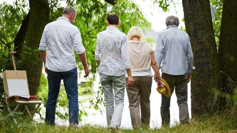 Group of seniors from behind go to a lake in summer