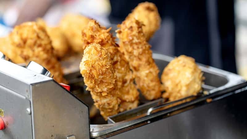 Closeup of golden crispy chicken strips frying in deep fryer. Breaded chicken pieces with crunchy coating during cooking process at street food stall.