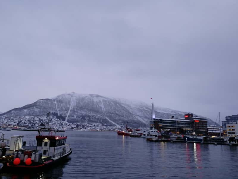 a snow capped mountain viewed from tromso harbour norway with fishing boats in the foreground
