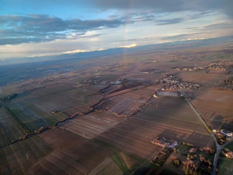 flat farmland with a rainbow and the alps mountains in the background from an aircraft on approach to trieste airport italy