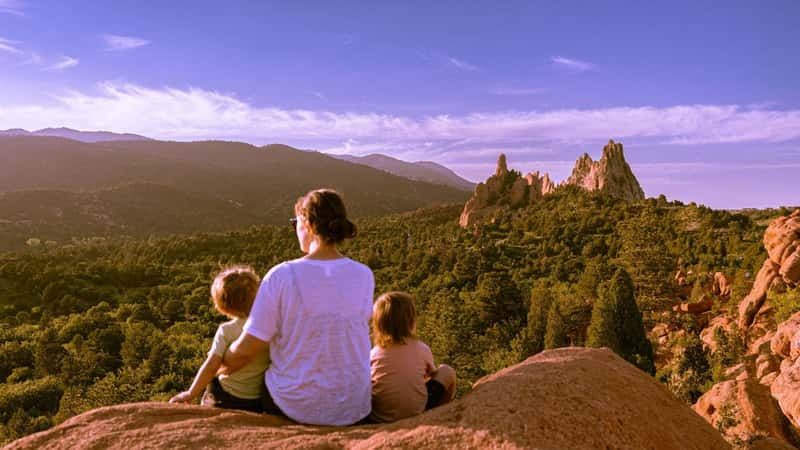 A parent and two young children sitting on a rock overlooking a mountainous landscape.