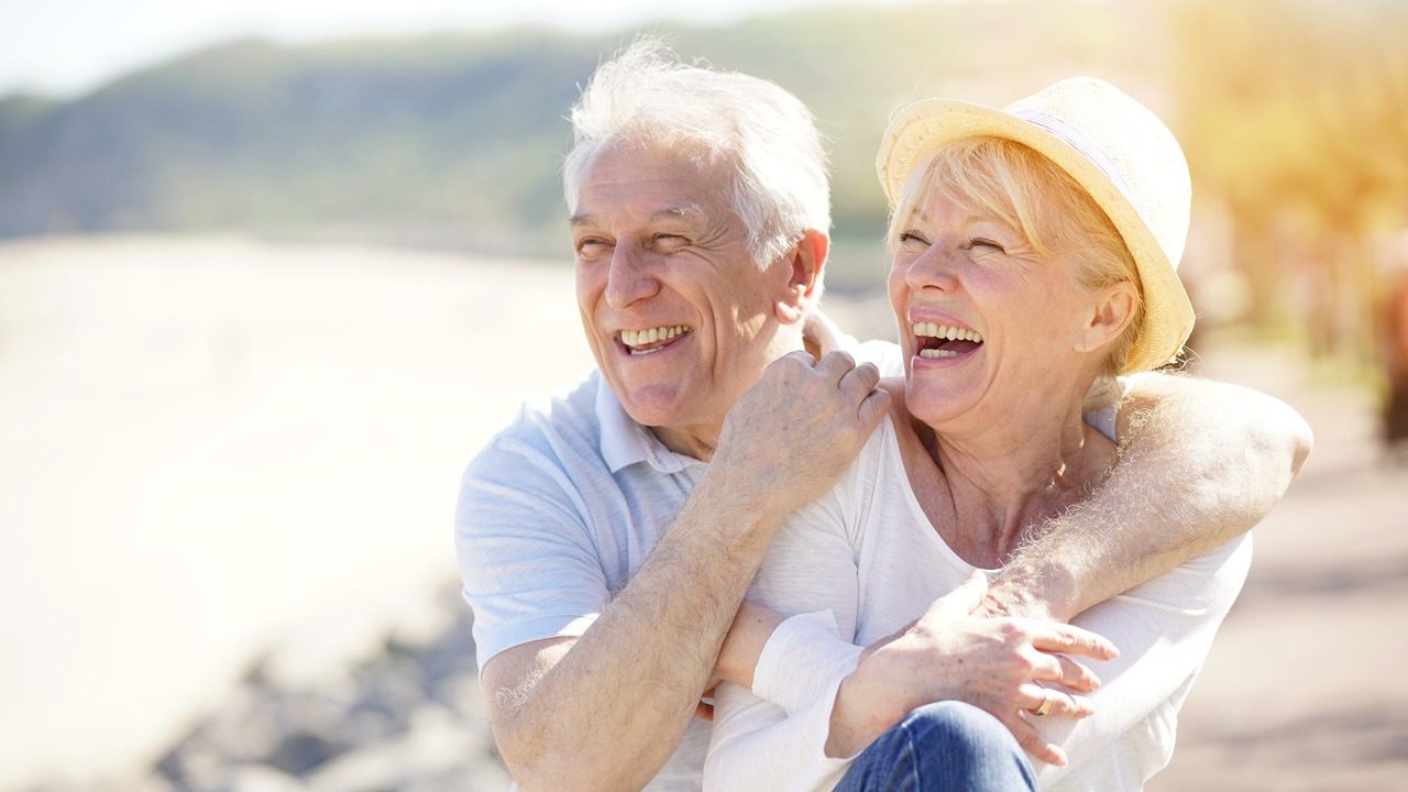 A retired couple smiling while standing near the ocean.