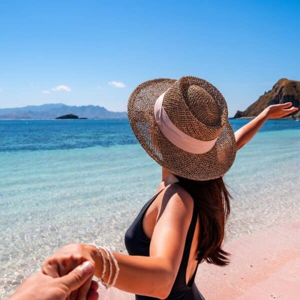 Young couple tourism enjoying the tropical pink sandy beach with clear turquoise water at Komodo islands in Indonesia